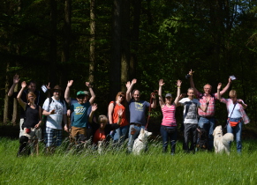 ChatGPT:  Auf dem Foto ist eine fröhliche Gruppe von Menschen zu sehen, die sich auf einer Wiese vor einem Wald versammelt hat. Alle Personen winken in die Kamera und wirken gut gelaunt. Die Gruppe besteht aus Männern, Frauen und Kindern – insgesamt etwa